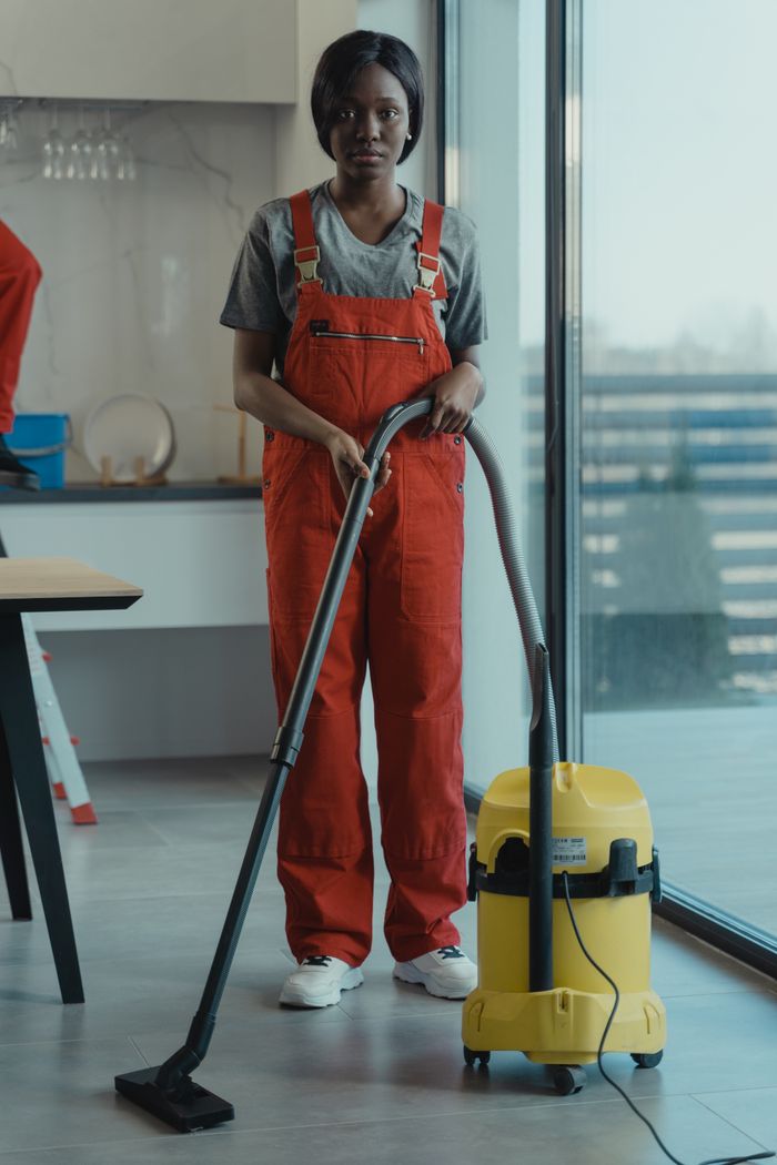 Une femme adulte en combinaison rouge utilise un aspirateur dans un environnement intérieur moderne, en se concentrant sur les tâches de nettoyage.
